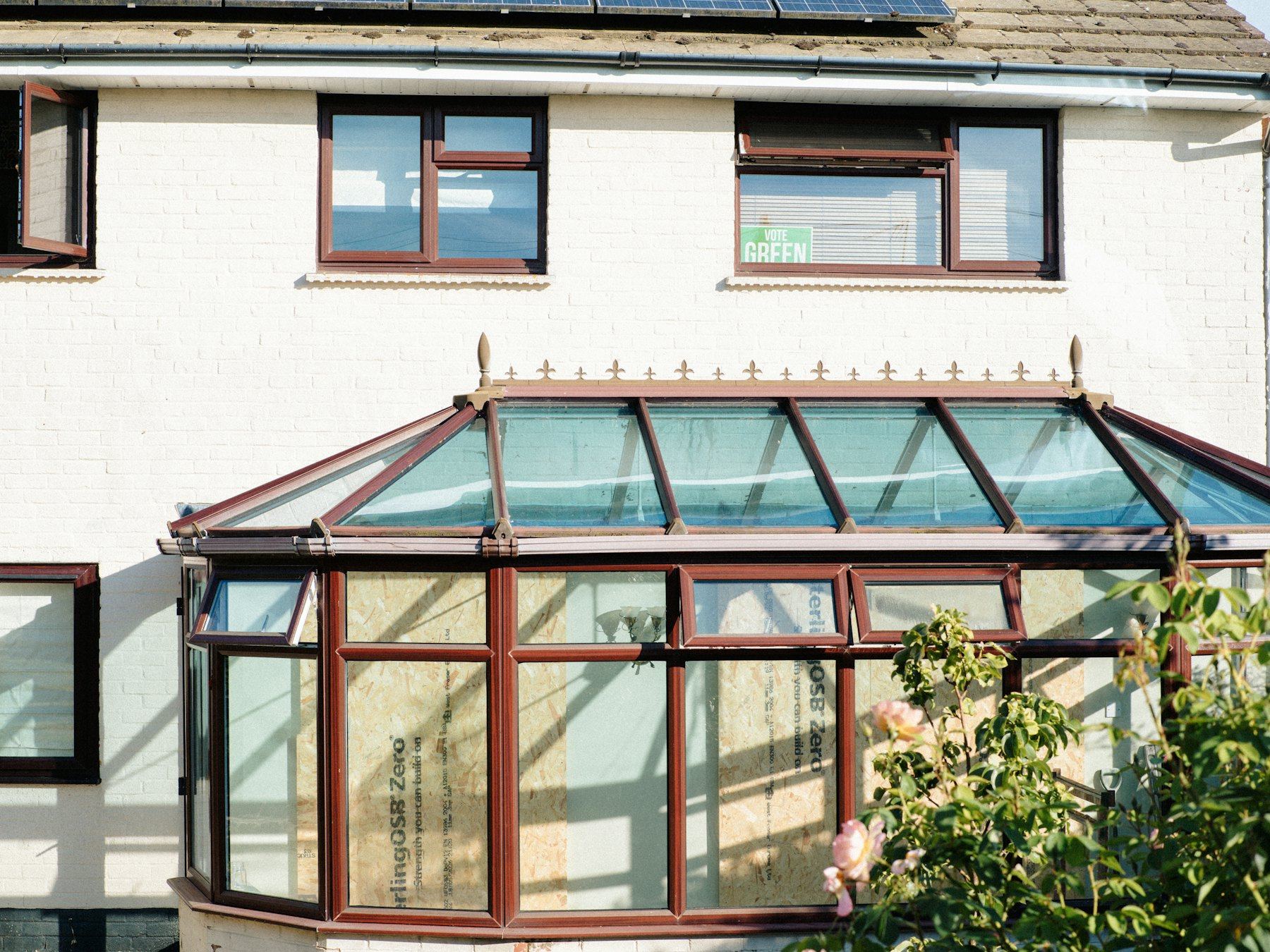 White house with a brown conservatory and solar panels on the roof.