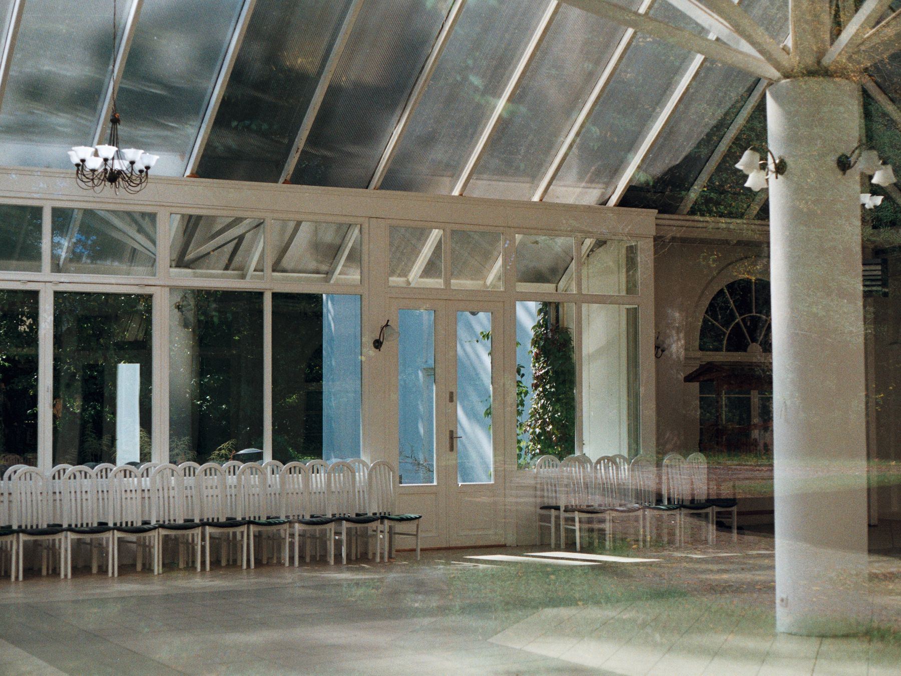 Double-exposed image of an empty conservatory with rows of white chairs.