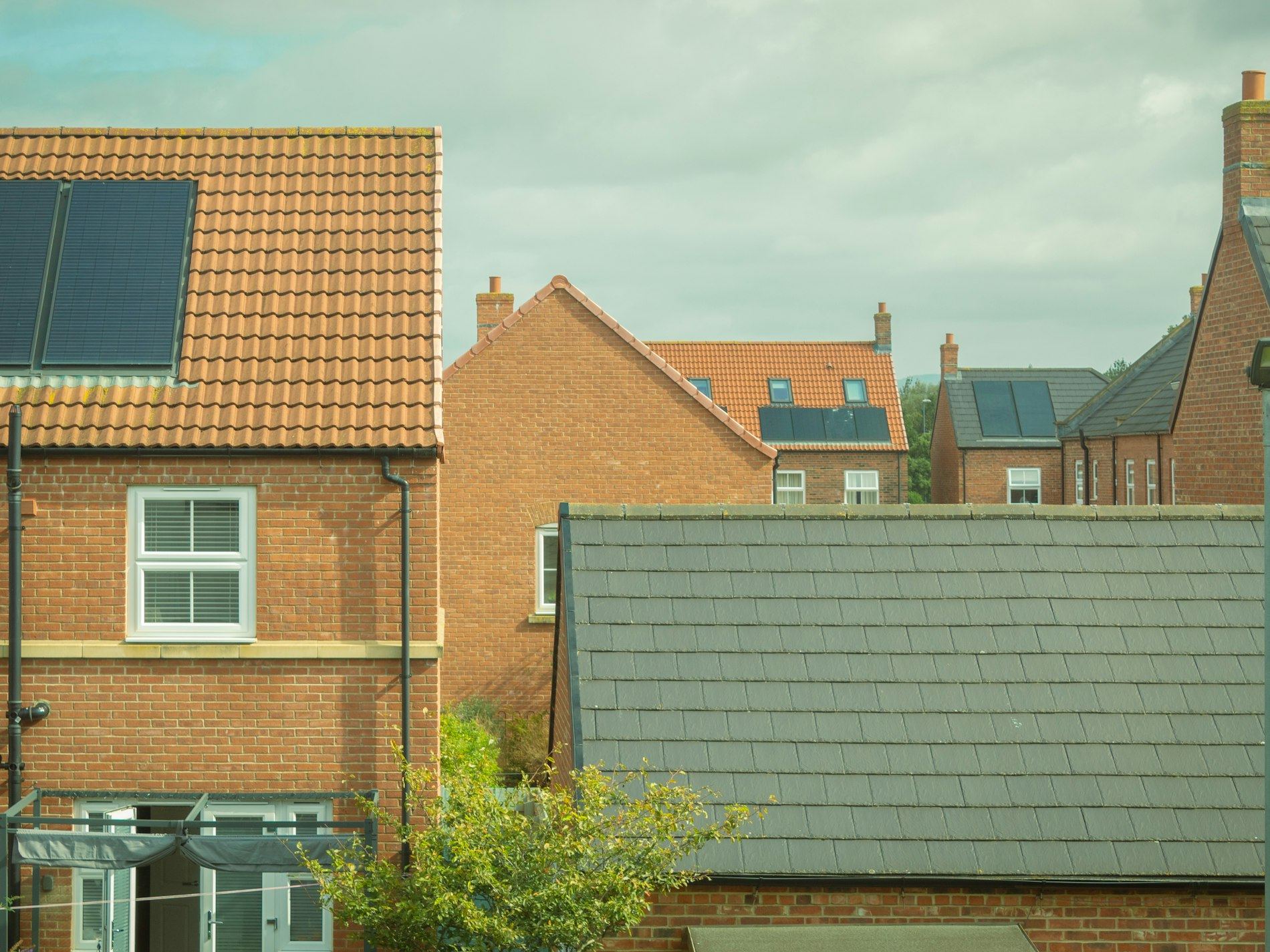 Rooftops of brick houses with solar panels under a cloudy sky.