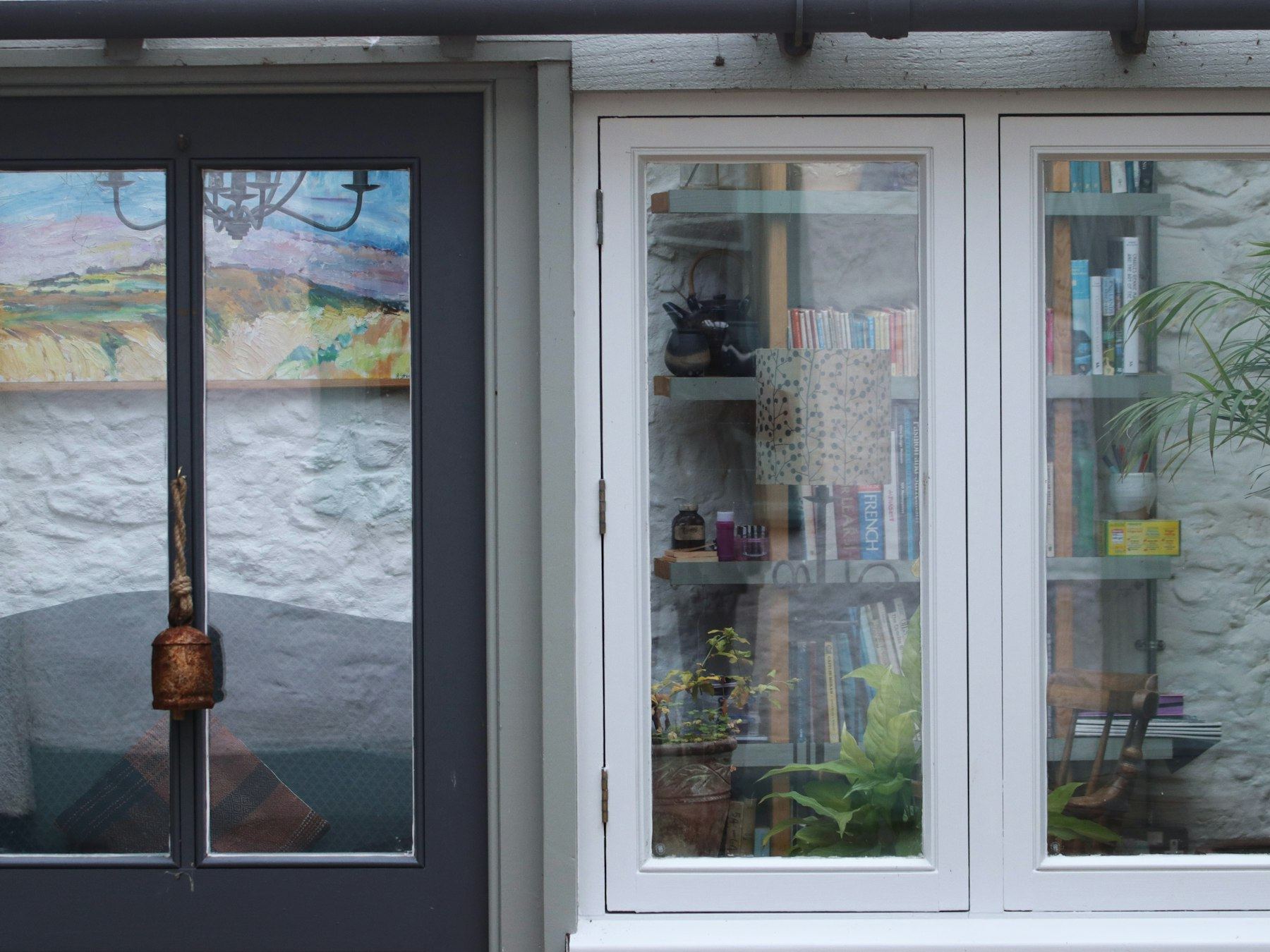 Dark door beside a white-framed window filled with books and plants.