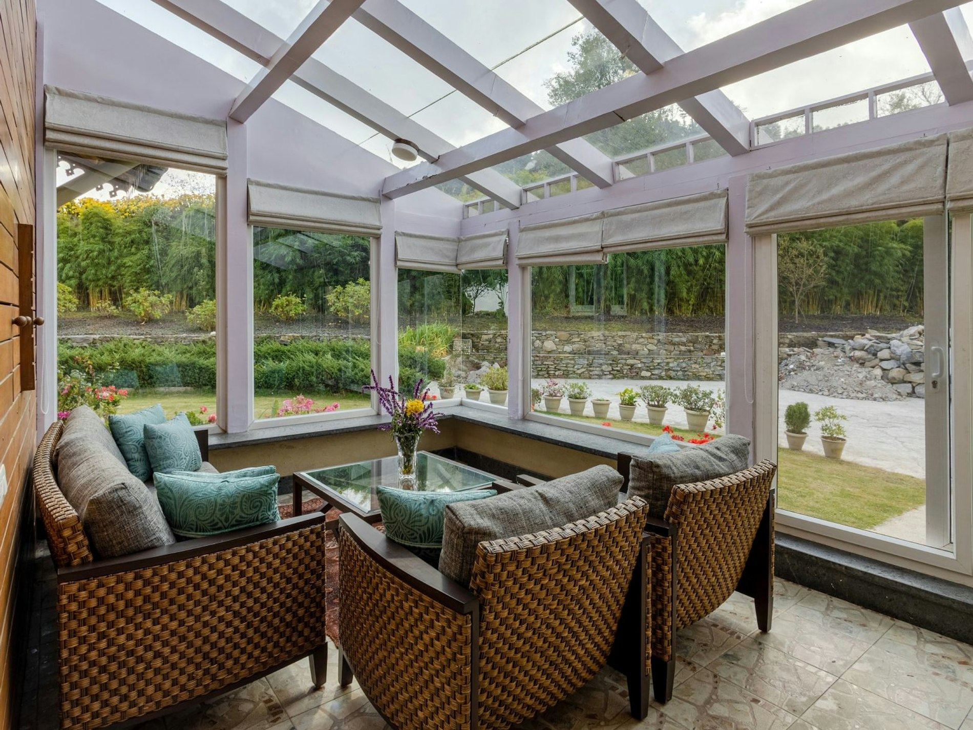 Bright conservatory with wicker armchairs and teal cushions overlooking a garden.
