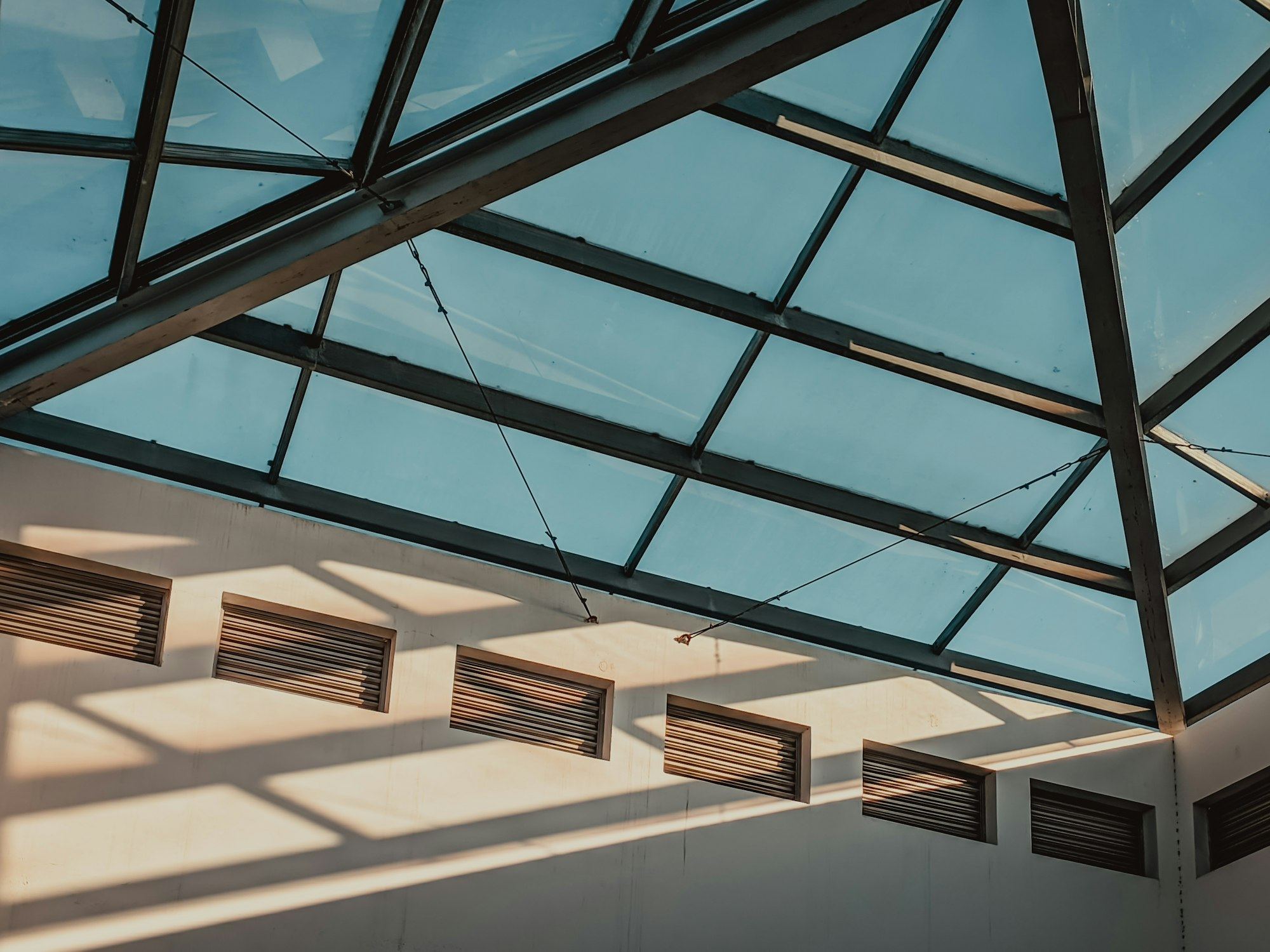 Interior view looking up at a glass conservatory roof with sunlight.