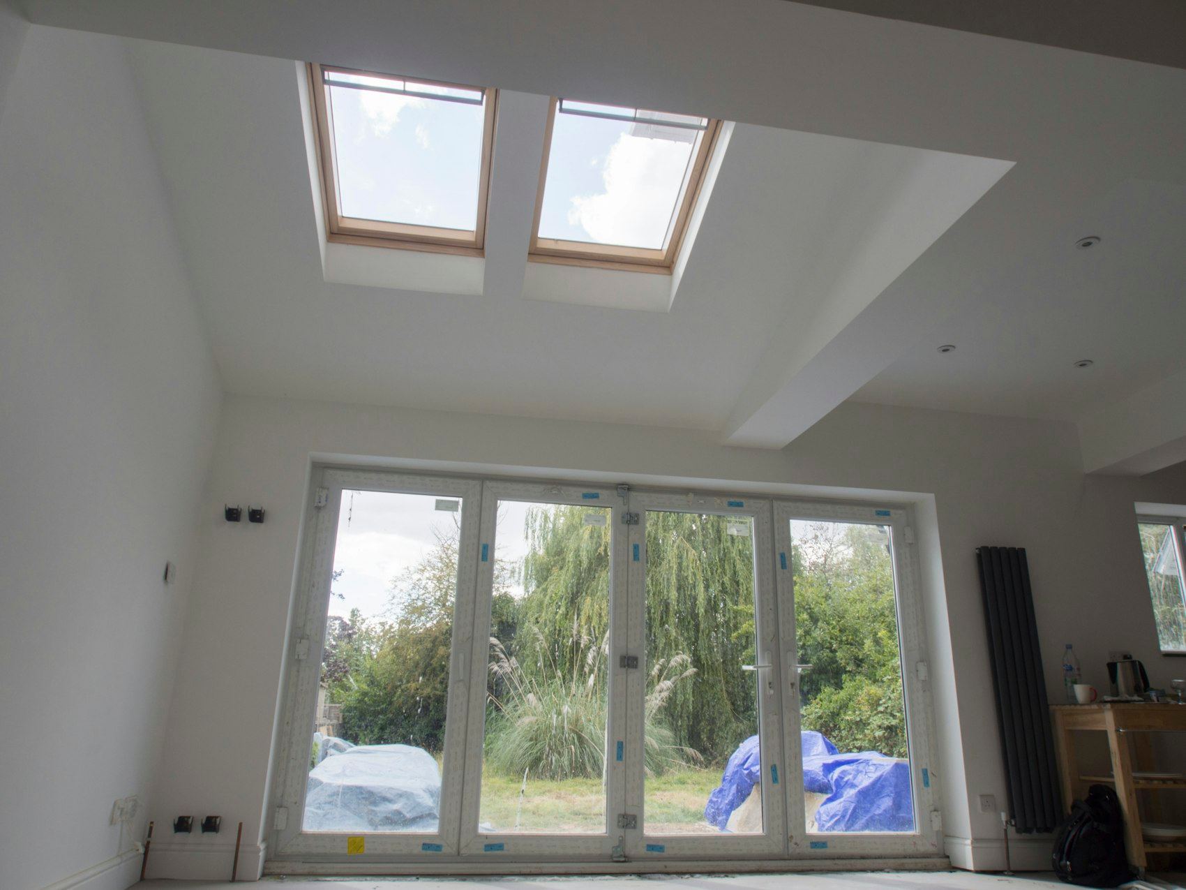Room under construction with skylights and bifold doors leading to a garden.